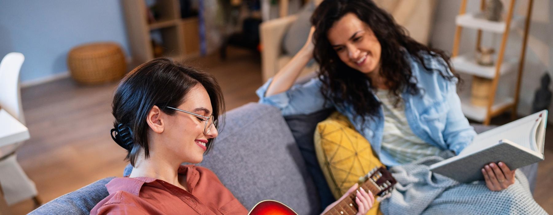 a person playing a guitar next to a person sitting on a couch